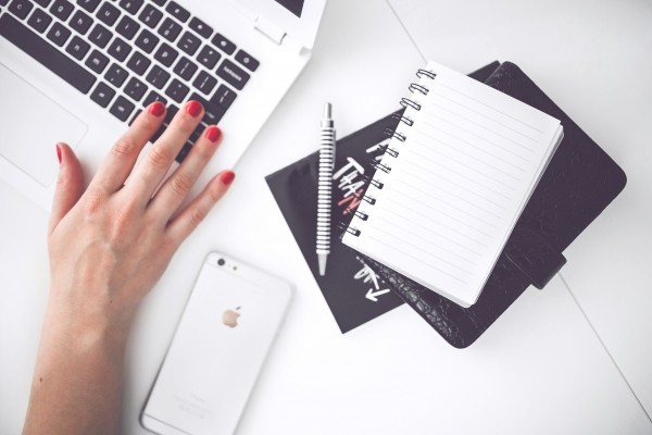 woman-working-on-laptop-with-notebook-and-mobile-phone-on-table